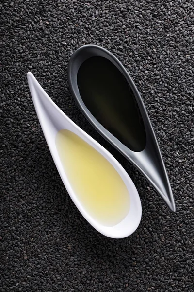 Sezamový olej v malých miskách na pozadí černého sezamu. — Stock fotografie