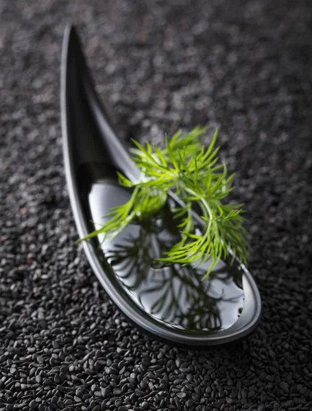 Plant oil  with dill branches on a background of black sesame. — Stock Photo, Image