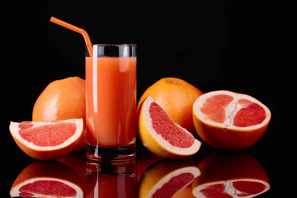 Glas Grapefruitsaft und geschnittene Früchte auf schwarzem Hintergrund. — Stockfoto