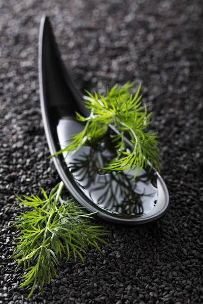 Aceite vegetal con ramas de eneldo sobre un fondo de sésamo negro . — Foto de Stock