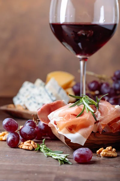 Gelas anggur merah dengan berbagai keju, buah-buahan dan prosciutto  . — Stok Foto