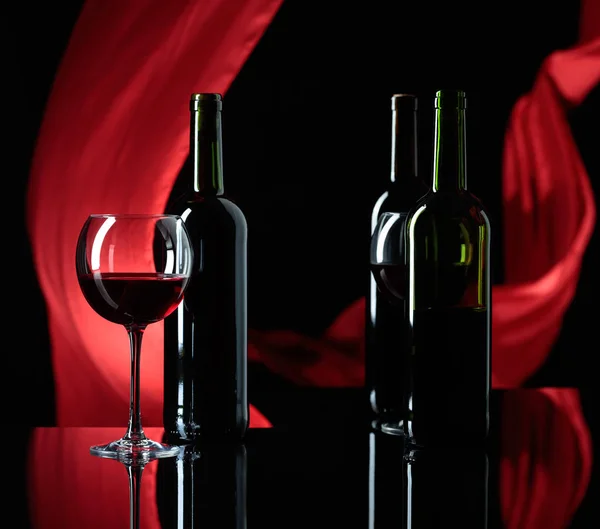 Weingläser und Rotweinflaschen auf schwarzem reflektierendem Backgr — Stockfoto