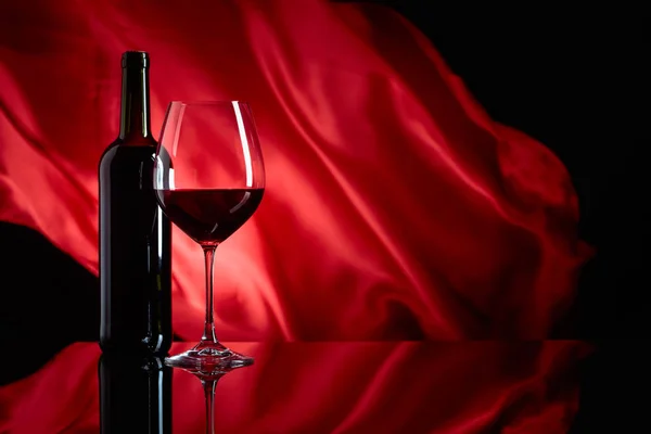 Borospohár és üveg vörösbor egy fekete reflektív háttérképet — Stock Fotó