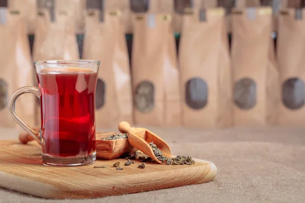 Szklany kubek z gorącą herbatą. Drewniana łyżka z suszonymi liśćmi herbaty. — Zdjęcie stockowe