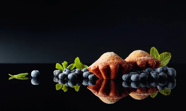 Magdalenas espolvoreadas con azúcar en polvo sobre un fondo negro reflectante —  Fotos de Stock