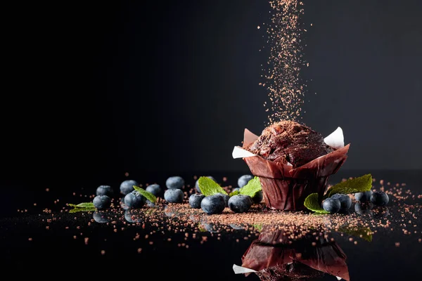 Muffin de chocolate espolvoreado con migas de chocolate en un refl negro —  Fotos de Stock