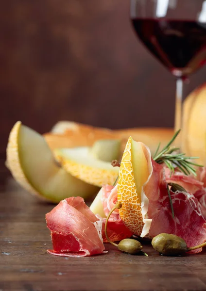 Prosciutto with melon, capers and rosemary on a old wooden tabl — Stock Photo, Image