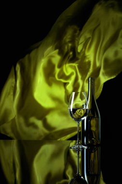 Wineglass and bottle of white wine on a black reflective backgro clipart