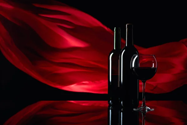 Weinglas und Rotweinflaschen auf schwarzem reflektierendem Hintergrund — Stockfoto