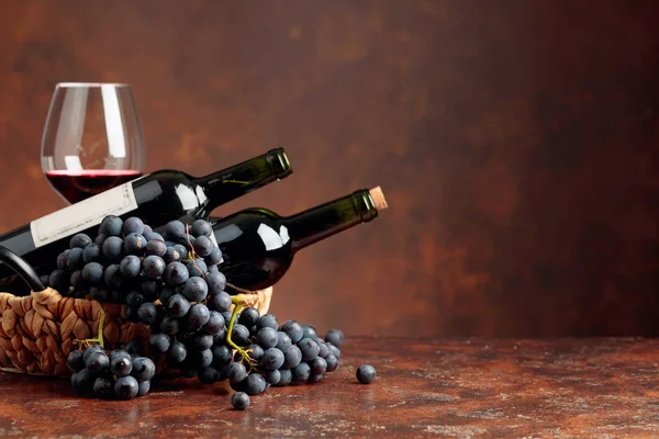 Juicy blue grapes and bottles of red wine on a brown background. — Stock Photo, Image