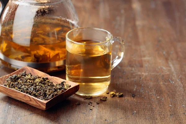 Thé vert chaud dans une tasse en verre. Feuilles de thé séchées et boisson chaude sur un — Photo