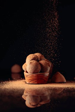Çikolatalı trüf mantarı kakao tozu serpiştirilmiş küçük ahşap tabakta.