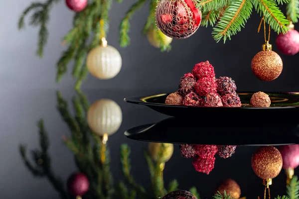 Chocolate truffles on a black plate and Christmas tree. — Stock Photo, Image