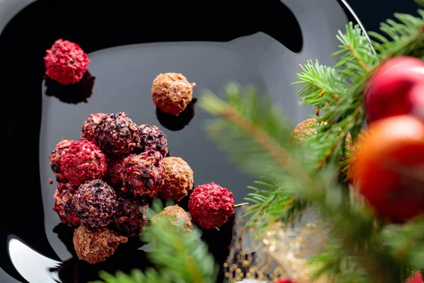 Diverses truffes au chocolat sur une assiette noire et un sapin de Noël. — Photo