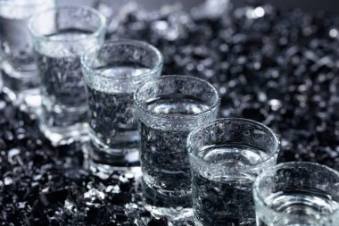 Damp glasses of vodka with ice on a black reflective background. clipart