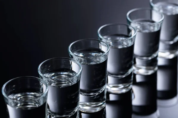 Vasos de vodka sobre fondo negro reflectante . — Foto de Stock