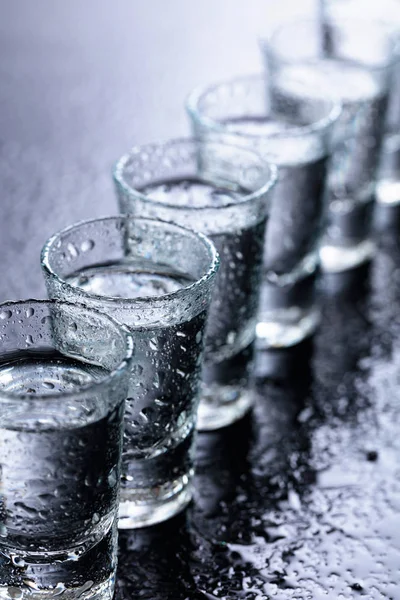 Szklanki wódki na wilgotnym szklanym stole. — Zdjęcie stockowe