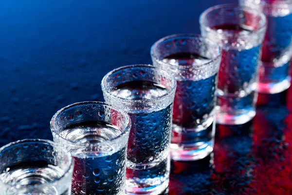 Vasos de vodka sobre una mesa de vidrio húmedo . — Foto de Stock