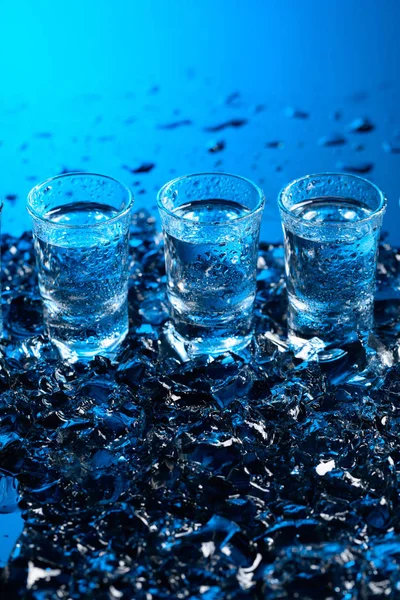 Damp glasses of vodka with ice on a black reflective background. — Stock Photo, Image