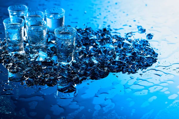 Bicchieri umidi di vodka con ghiaccio su uno sfondo riflettente nero . — Foto Stock