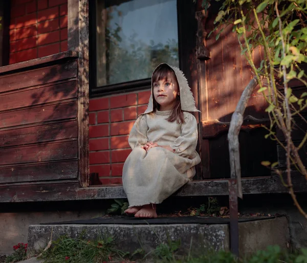 Little girl in a old canvas dress on the threshold of the house. — Stock Photo, Image