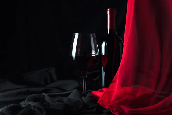 黒絹の背景に赤ワインのボトルとガラス. — ストック写真