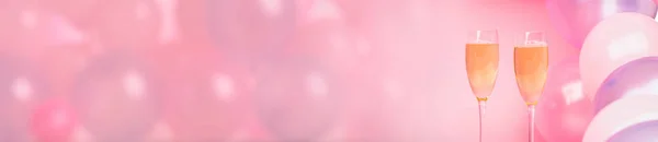 Two glasses of champagne on a pink background with pink balloons