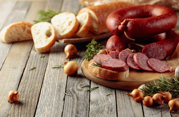 На старом деревянном столе колбаса с хлебом, розмарин, лук и пе — стоковое фото