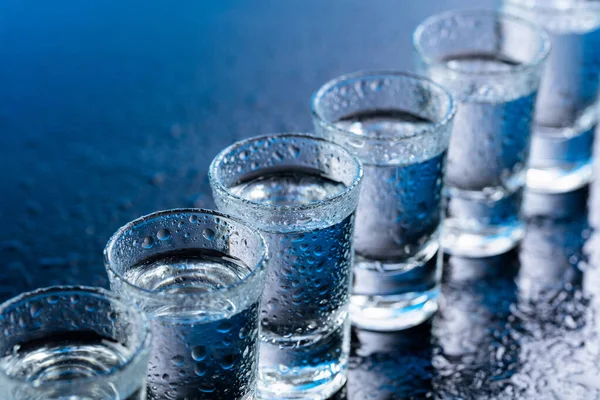 Vasos de vodka sobre una mesa de vidrio húmedo . —  Fotos de Stock