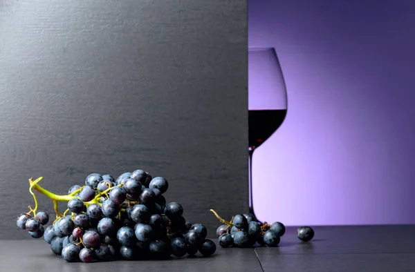 Rödvin druvor på ett svart bord och glas rött vin. — Stockfoto