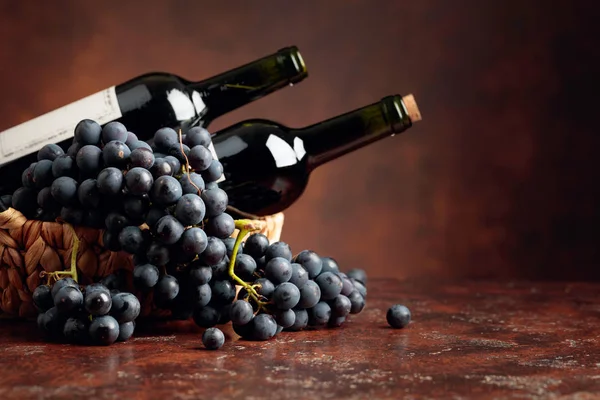 Juicy blue grapes and bottles of red wine on a brown background. — Stock Photo, Image