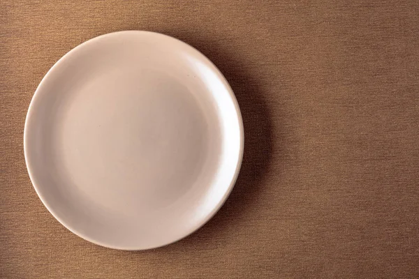 Assiette ronde vide en céramique beige sur une nappe beige . — Photo