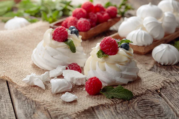 Pavlova und kleine Baiser auf rustikalem Holzgrund. — Stockfoto