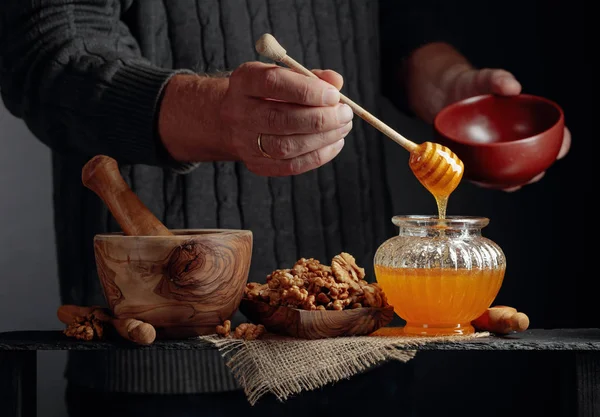 Man in a sweater prepares a breakfast of walnuts and honey. — Stock Photo, Image