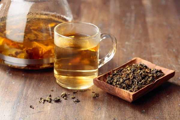 Thé vert chaud dans une tasse en verre. Feuilles de thé séchées et boisson chaude sur un — Photo