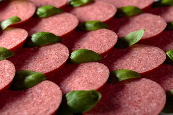 Sliced smoked sausage with green basil leaves. — Stock Photo, Image