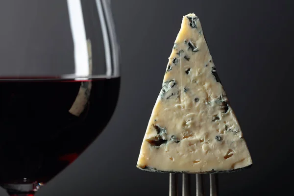 Piece of blue cheese on a fork and red wine. — Stock Photo, Image