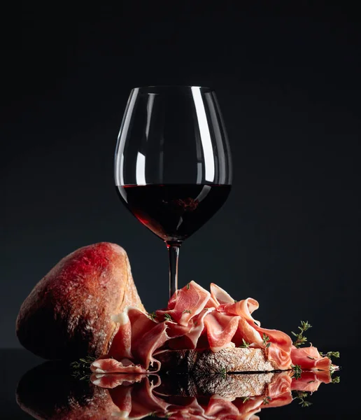 Prosciutto com ciabatta, vinho tinto e tomilho em um backgrou preto — Fotografia de Stock