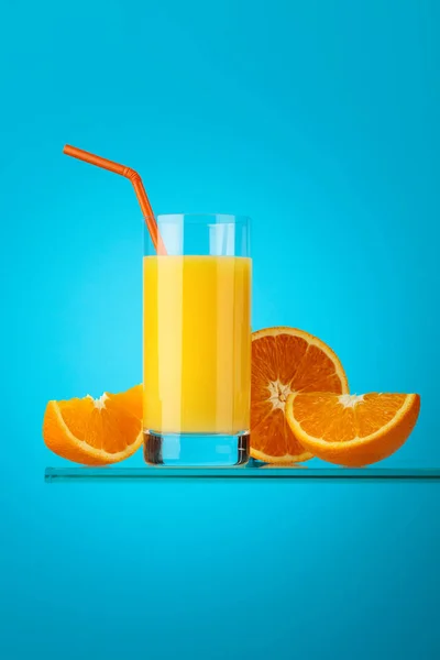 Vaso de zumo de naranja con frutas frescas sobre fondo azul . — Foto de Stock