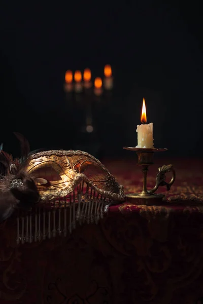 Hořící svíčka v malém mosazném svícnu a staré karnevalové masce — Stock fotografie