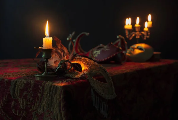 Płonąca świeca w małym mosiężnym świeczniku i starych maskach karnawałowych — Zdjęcie stockowe
