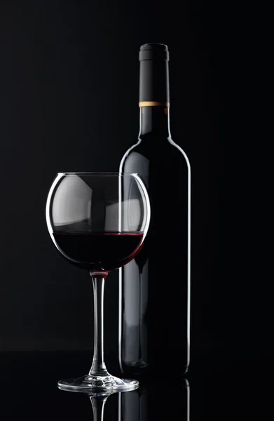 Garrafa e copo de vinho tinto sobre fundo preto. — Fotografia de Stock