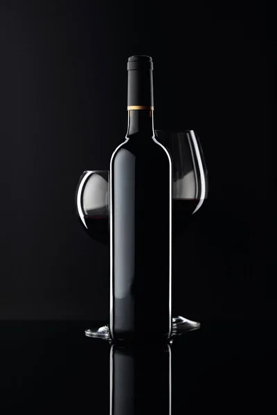 Botella y copas de vino tinto sobre fondo negro . — Foto de Stock
