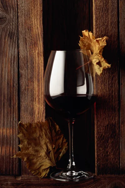 Vaso de vino tinto y hojas de vid seca sobre fondo de madera . —  Fotos de Stock