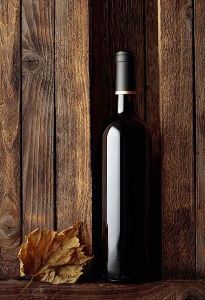 Garrafa de vinho tinto e folha de videira seca em um velho backgroun de madeira — Fotografia de Stock