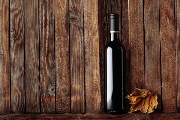 Bir şişe kırmızı şarap ve kurumuş asma yaprağı eski bir ahşap grupta — Stok fotoğraf