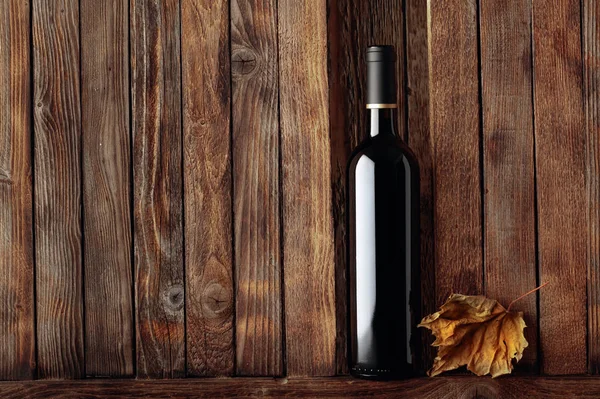 Botella de vino tinto y hoja de vid seca sobre un viejo fondo de madera —  Fotos de Stock