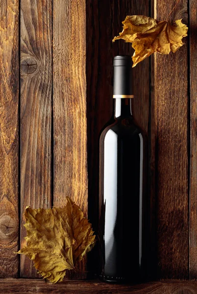 Garrafa de vinho tinto e folhas de videira secas em um velho backgro de madeira — Fotografia de Stock
