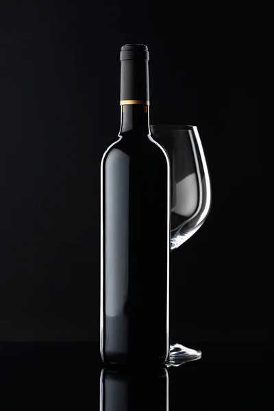 Botella de vino tinto y vaso vacío sobre fondo negro . — Foto de Stock