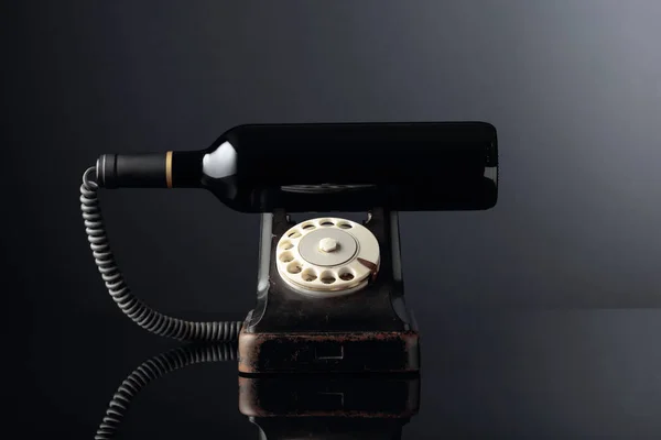 Telefone preto velho e garrafa de vinho tinto em um bac reflexivo preto — Fotografia de Stock